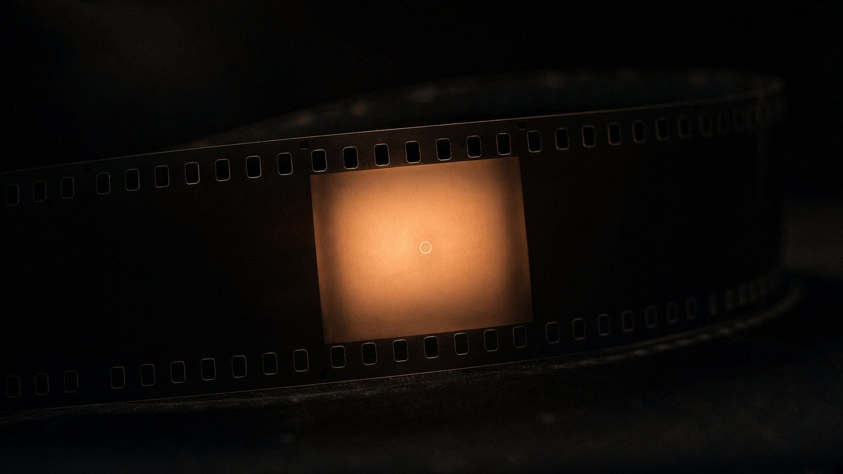 A strip of blank 16 mm film, one frame lit from behind with a tiny bright ring